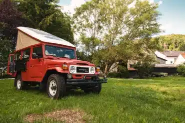 Roter Toyota Land Cruiser BJ45 mit ausgefahrenem Hubdach als Campingfahrzeug auf einer Wiese