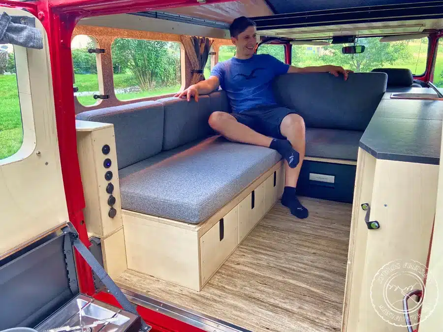Innenausbau eines Toyota Land Cruiser BJ45 mit L-förmiger Sitzbank, grauen Polstern, Holzschubladen und Küchenzeile