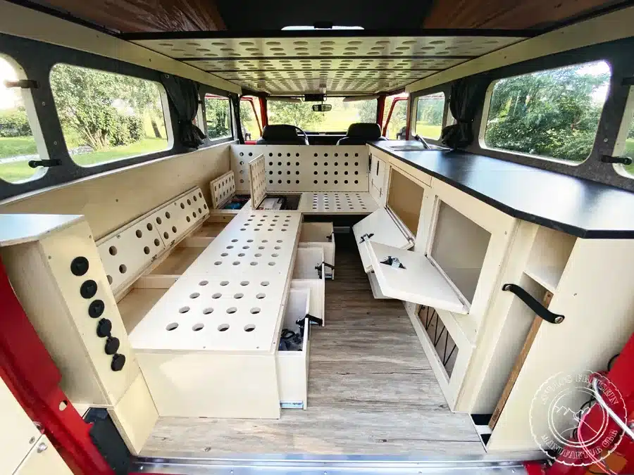 Innenraum eines ausgebauten Toyota Land Cruiser BJ45 als Camper mit L-förmiger Küchenzeile, Sitzbänken und Stauraumfächern.