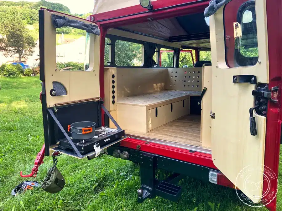 Innenausbau eines Toyota Land Cruiser BJ45 mit offener Heckklappe, Sitzbänken und ausklappbarem Kochfeld.