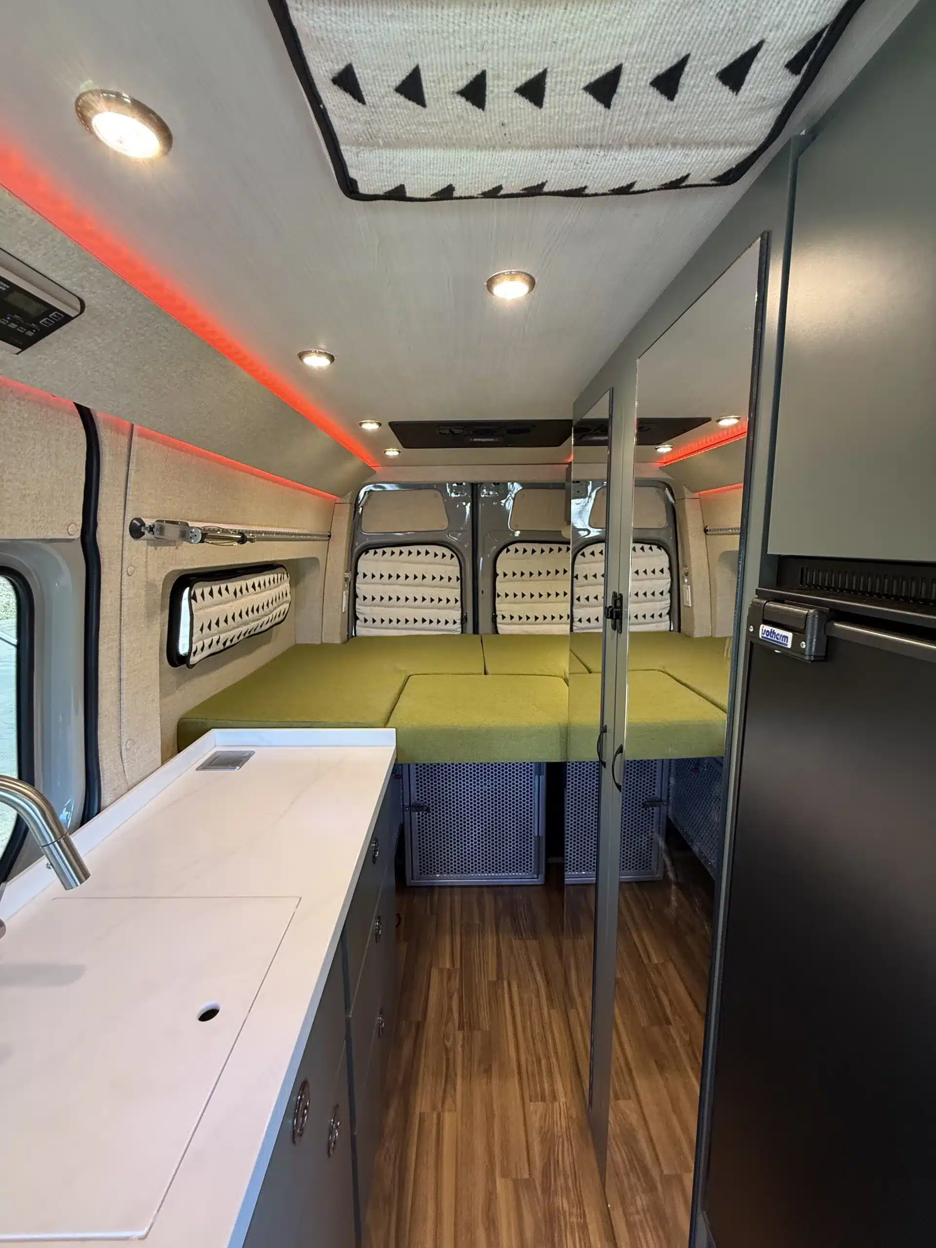 Innenausstattung eines Trail-Hob Kastenwagens mit Plattformbett, Küchenzeile und Stauraum, ausgelegt für zwei Personen und Hunde.