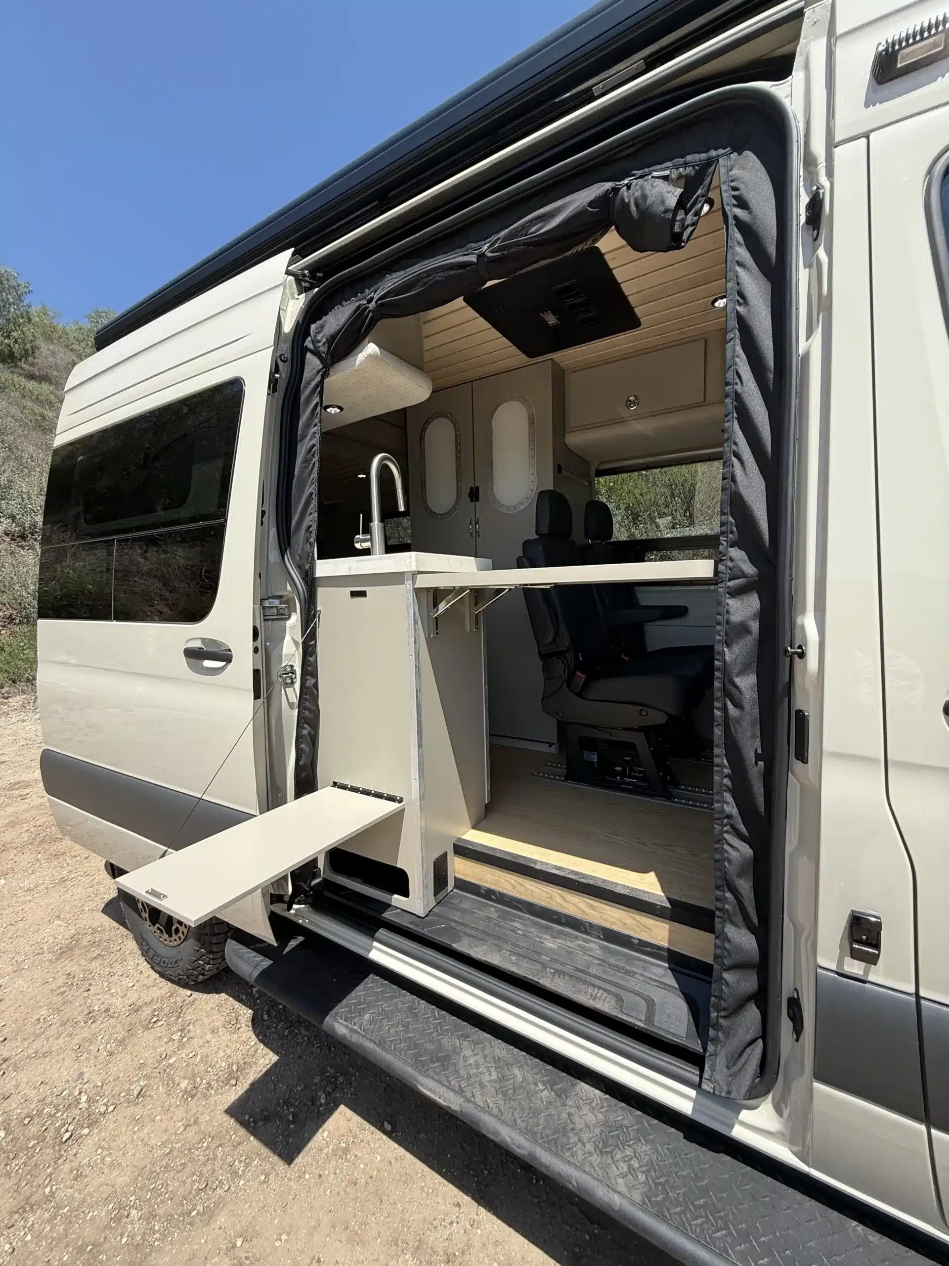 Trail Hob Campervan mit geöffneter Schiebetür, Küchenbereich und Klapptisch vor natürlicher Kulisse