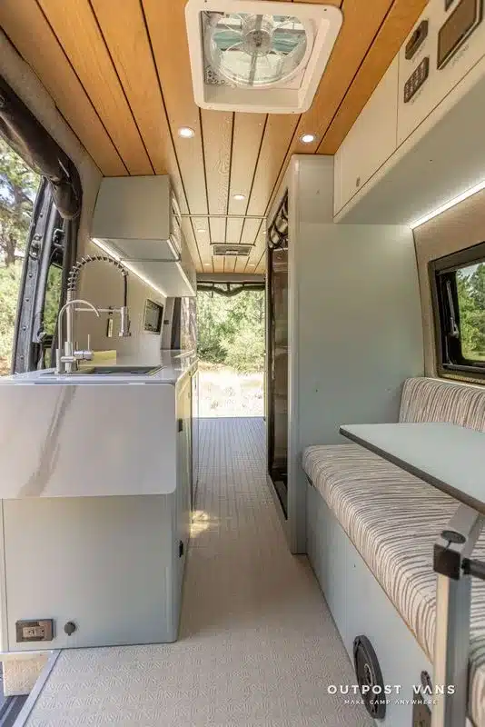 Küche und Wohnbereich eines ausgebauten Mercedes-Benz Sprinter Campervans mit moderner Inneneinrichtung, Holzhimmel und Sitzbank.