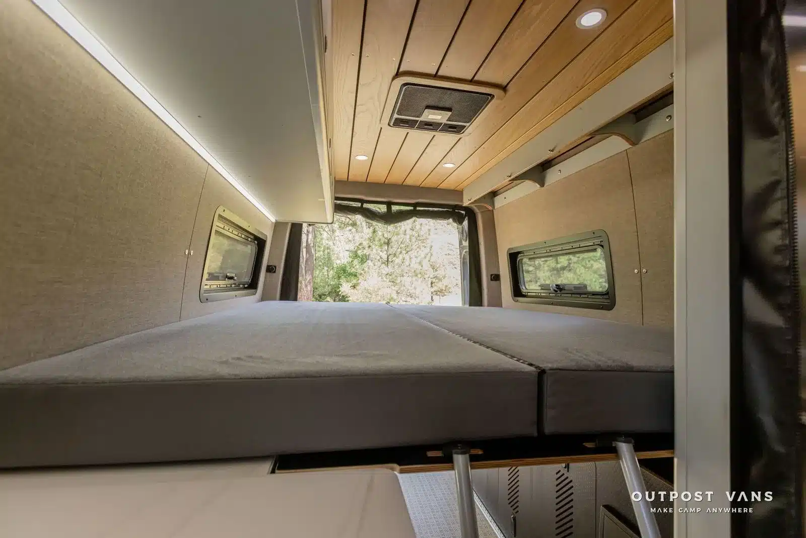 Innenansicht eines UNCHAINED Sprinter Campervans mit ausgeklapptem Murphy-Bett, Holzdecke und seitlichen Staufächern.