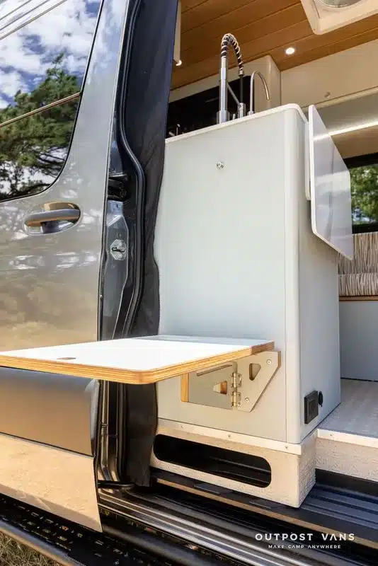 Küchenblock mit Spüle und ausklappbarem Tisch im Campervan an geöffneter Schiebetür