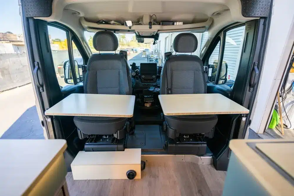 Fahrerhaus eines Kastenwagens mit drehbaren Sitzen und montierten Tischen, Teil des Avalon Campervan-Ausbaus.