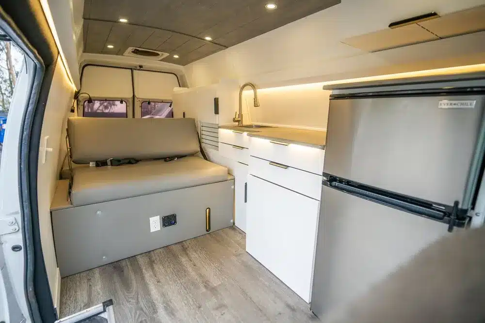 Innenansicht des Turq Campervans mit Küchenblock, Kühlschrank und Sitz-/Schlafbereich aus Aluminium und Holz