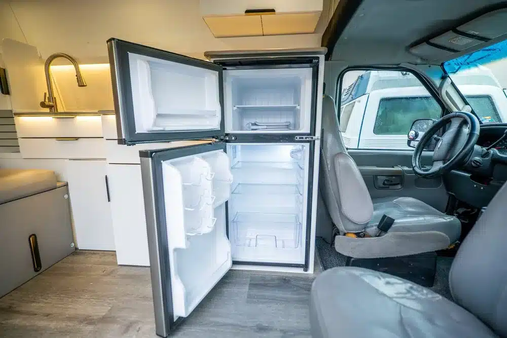 Geöffneter 12-Volt-Kühlschrank im Innenraum eines Vamonos Vans Turq Campers mit moderner Küchenzeile