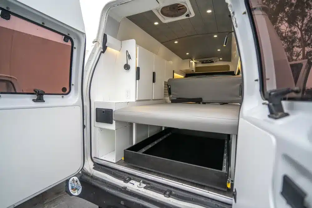 Innenansicht des Turq Campervans von Vamonos Vans mit Ausziehbett, weißen Aluminiumschränken und Stauraum.