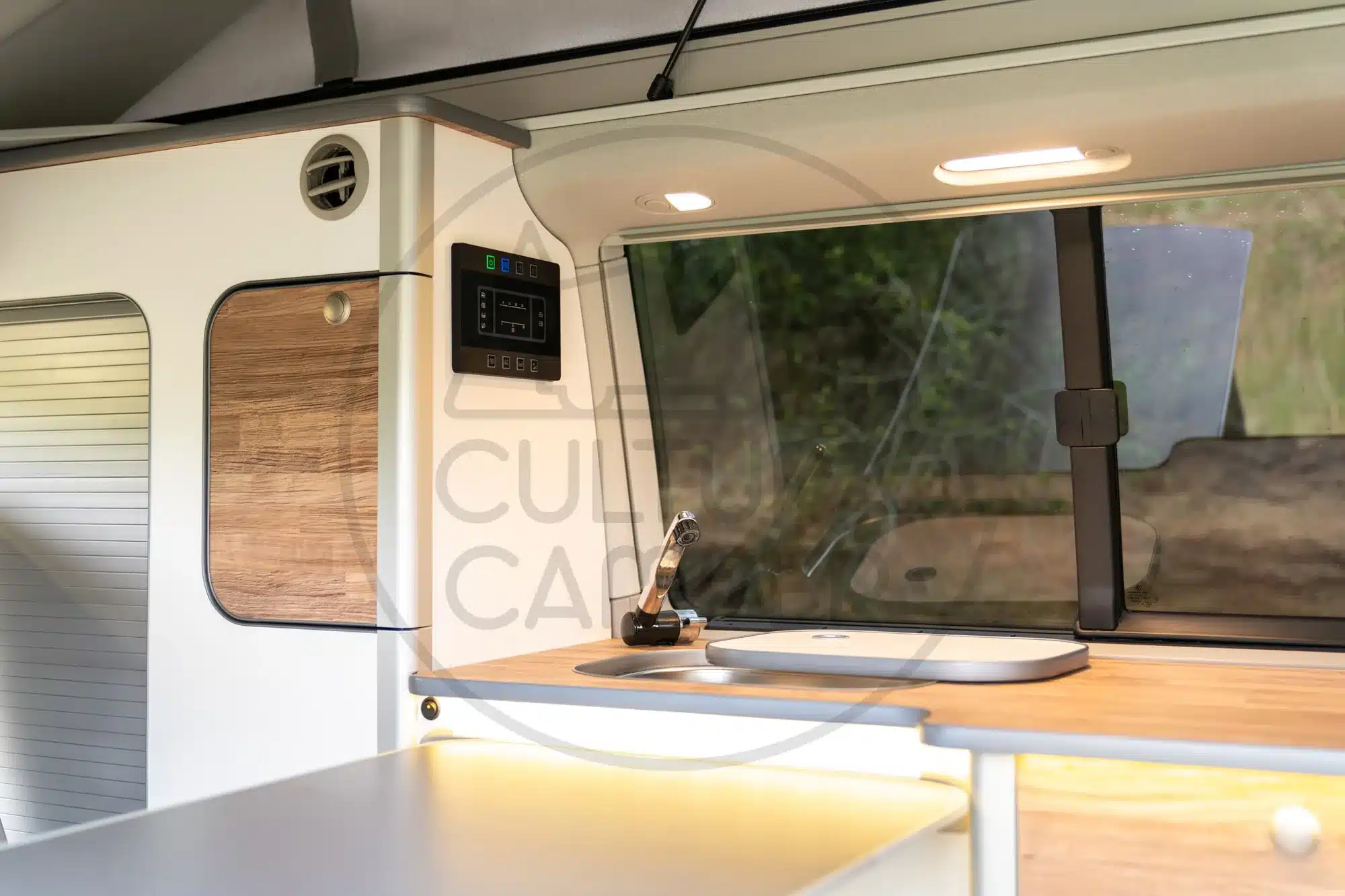 Innenraum eines VW T6 California mit maßgefertigter Küchenzeile, modernen Möbeln und Technikpanel