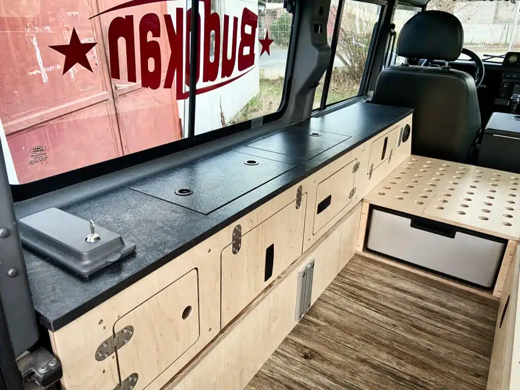 Innenraum eines Land Rover Defender mit Camper-Ausbau, Längsbank und Küchenzeile aus Holz