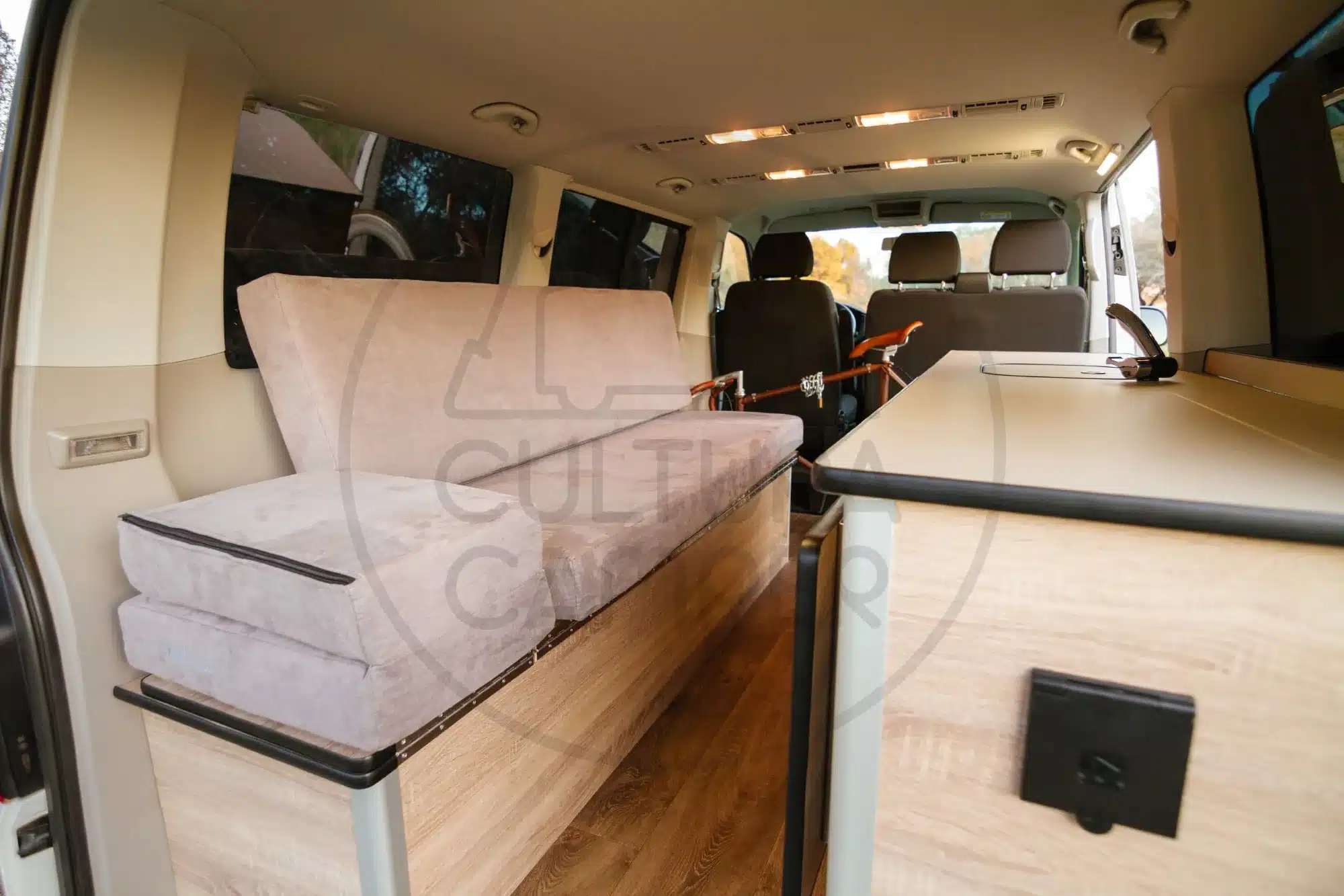 Innenraum eines individuell ausgebauten VW Caravelle T6 mit Sitz-/Schlafbereich, Stauraum und Küchenzeile