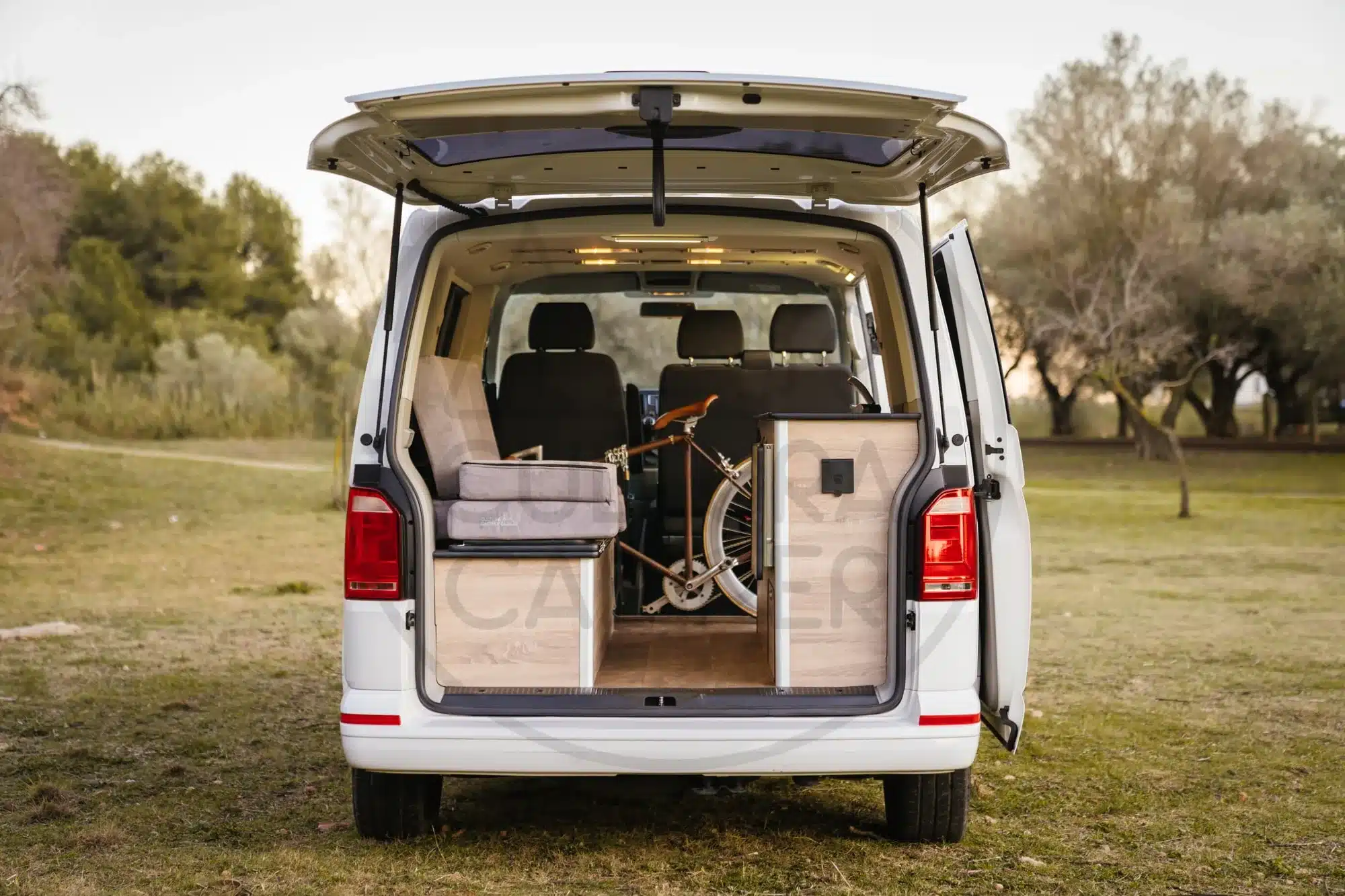 Offener Heckbereich eines VW Caravelle T6 mit individuell ausgebautem Innenraum, Stauboxen und einem gesicherten Fahrrad.