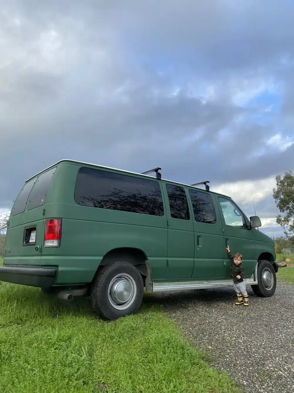 Grüner, ausgebauter Ford E350 Van steht auf einer Wiese, ein Kind steht an der Seitentür