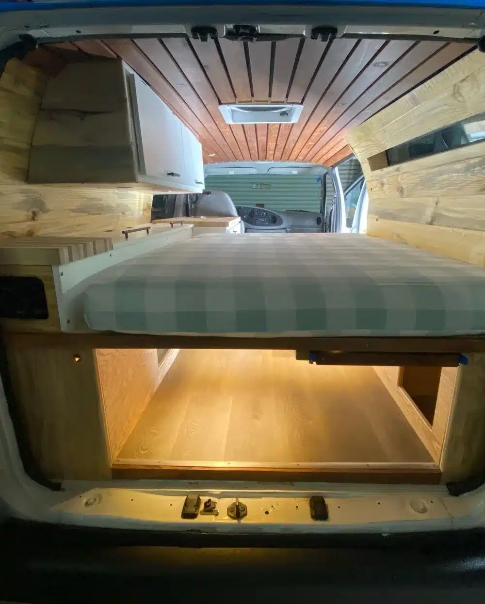 Innenraum eines ausgebauten Campervans mit Bett, Holzverkleidung und großzügigem Stauraum
