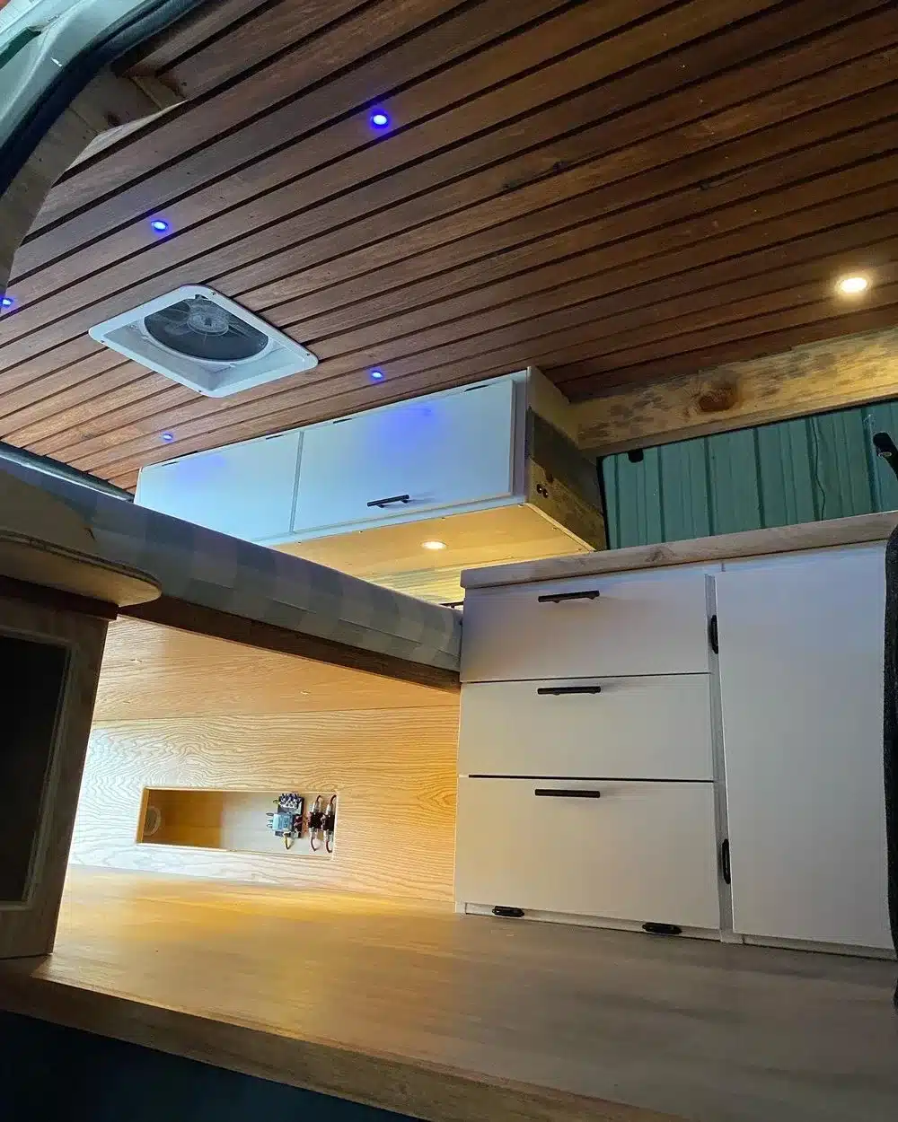 Detailansicht des Innenausbaus eines Ford E350 Campervans mit Holzdecke, LED-Spots, Oberschrank, Sofa-Bett und Küchenmodul.