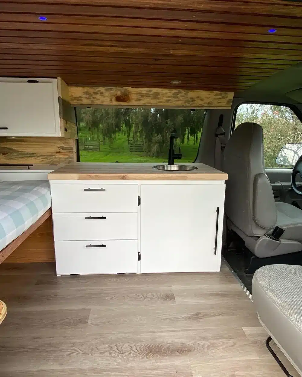 Kompakte Küchenzeile mit weißem Unterschrank, Spüle und Holzakzenten im Innenraum eines Campervans