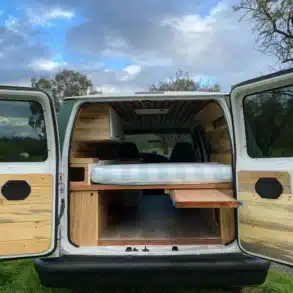 Blick in den ausgebauten Ford E350 Camper mit offener Heckklappe, Stauraum und Polsterbett.
