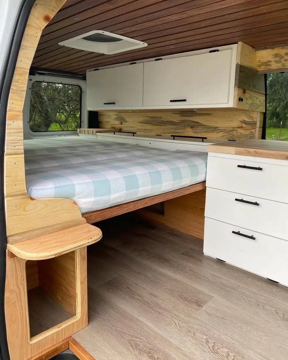 Innenraum des Wrigley Wintergreen Campervans mit Bett, weißen Staufächern und Holzverkleidung