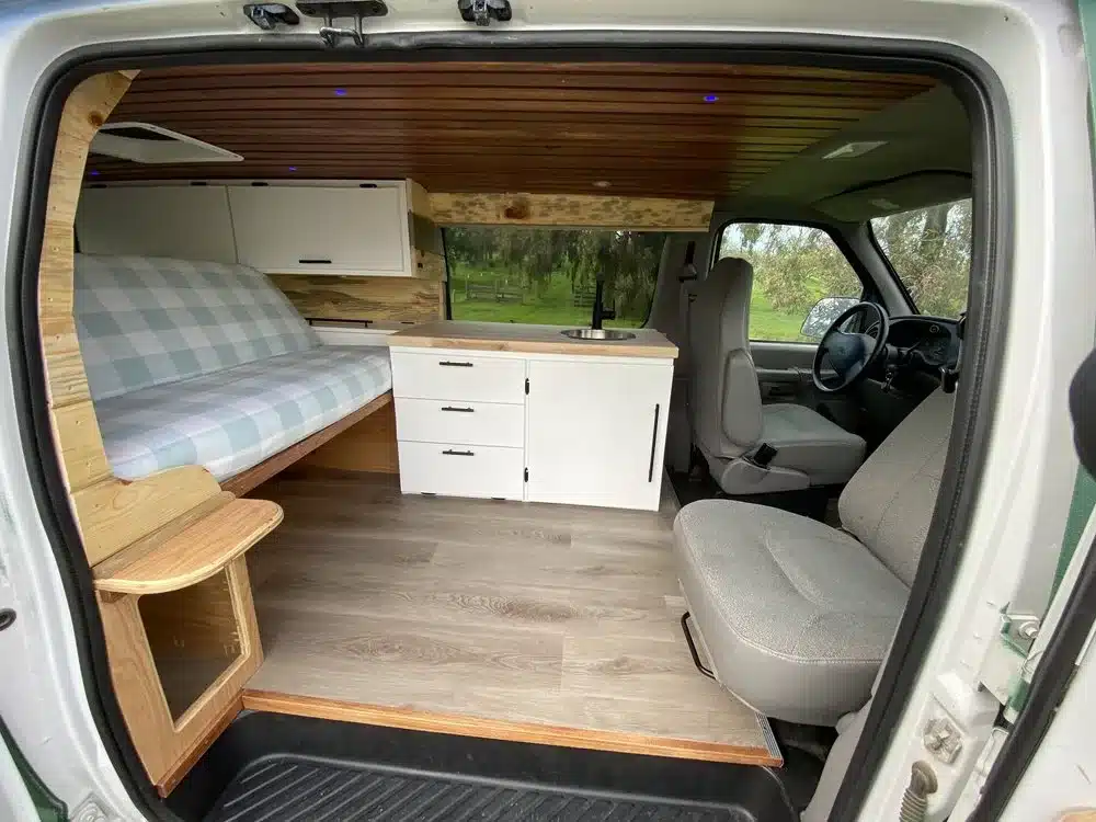 Innenraum eines ausgebauten Ford E350 Vans mit Bett, Küchenzeile und drehbarem Sitz.