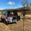 Heckansicht des Brooklyn J69JL Campervans mit ausgeklappter Markise und geöffneten Türen im trockenen Grasland.