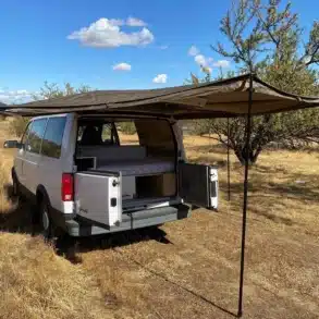 Heckansicht des Brooklyn J69JL Campervans mit ausgeklappter Markise und geöffneten Türen im trockenen Grasland.