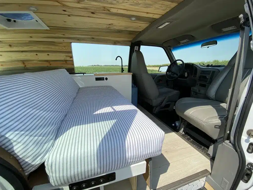 Innenansicht des Brooklyn J69JL Campervans mit Streifensofa, Fahrerkabine und hellem Holzausbau