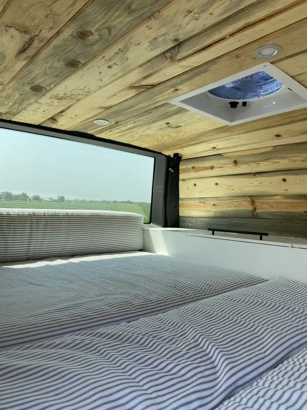 Schlafbereich mit gestreifter Bettwäsche und Holzdecke im Brooklyn J69JL Campervan