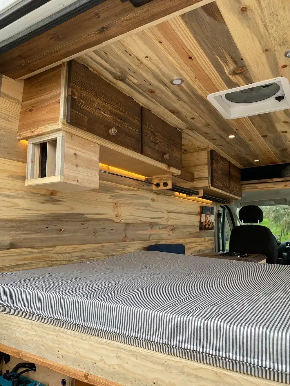 Innenraum des Yolo Cozy Cabin Camperausbaus mit Holzdekor, Stauraum und Bett