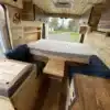 Camperinnenraum des Yolo Cozy Cabin mit gemütlichem Holzausbau, variablem Bett und Sitzplätzen.