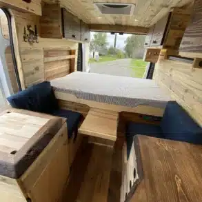 Camperinnenraum des Yolo Cozy Cabin mit gemütlichem Holzausbau, variablem Bett und Sitzplätzen.
