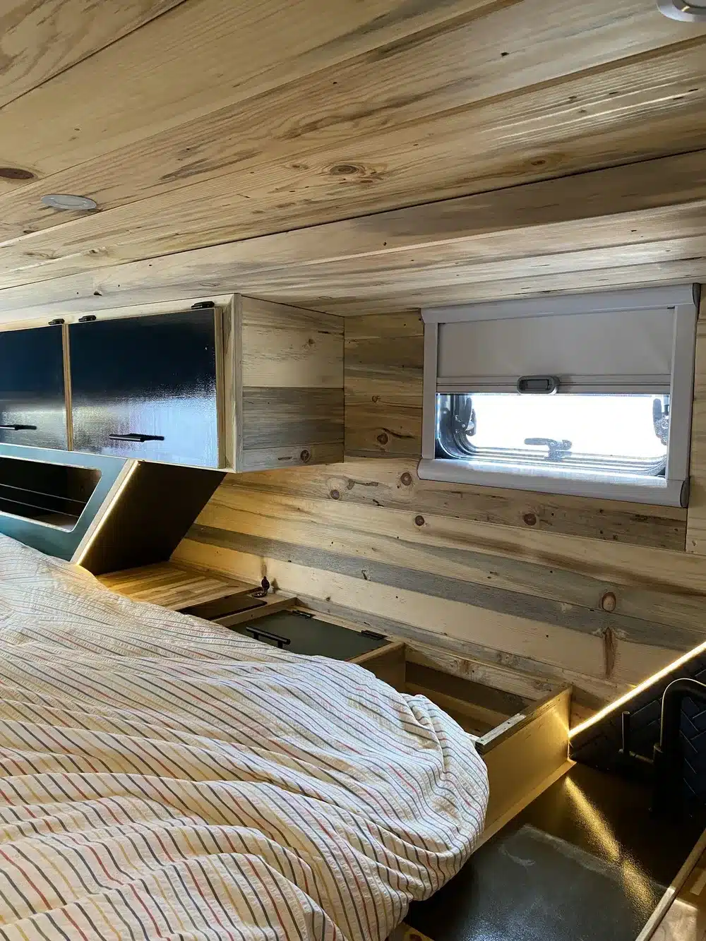Innenraum einer zum Camper umgebauten Ambulanz mit Holzverkleidung, Stauraum und Schlafbereich