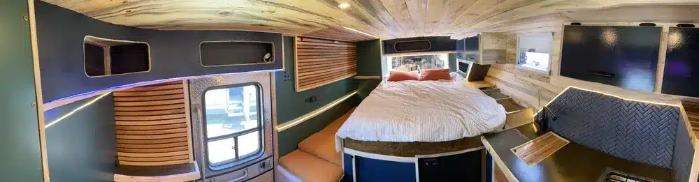Panoramaaufnahme des Innenbereichs einer zum Camper umgebauten Ambulanz namens Fambulance, mit Bett, Sitzgelegenheiten und Stauraum.