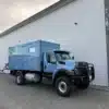 Bliss Mobil 16-Fuß-Expeditionskabine auf einem blauen 4x4-Lkw vor moderner Halle