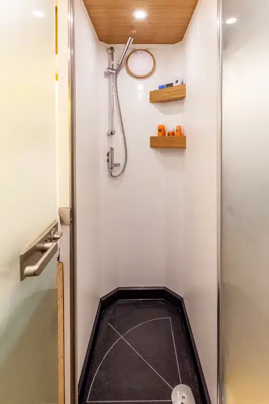 Duschkabine mit Handbrause und zwei Wandregalen im Bliss Mobil Expeditionsfahrzeug