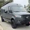 Grauer Mercedes Sprinter 170 4x4 Campervan mit Offroad-Setup und Markise auf einer Straße