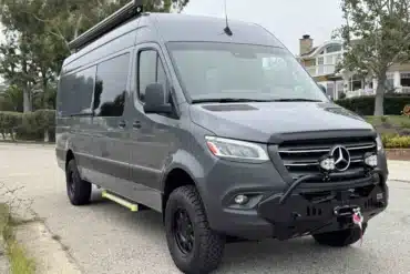 Grauer Mercedes Sprinter 170 4x4 Campervan mit Offroad-Setup und Markise auf einer Straße