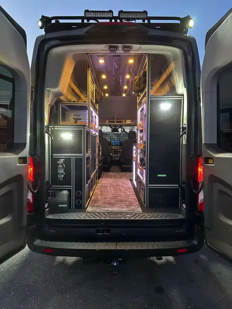 Innenraum eines 2022 Ford Transit 350 HR PASS XL mit Ausbau zum Overland-Van, beleuchtet und mit viel Stauraum.