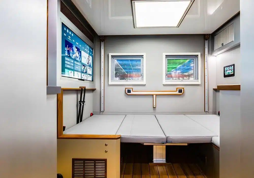 Innenansicht des 2025 U3 Unimog Expedition Campers mit ausgeklapptem Bett, zwei Fenstern und Bildschirm.