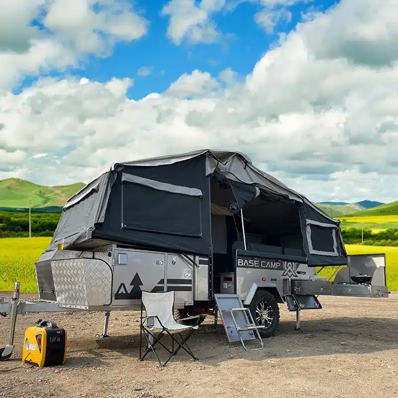 Base Camp 3C Tent Trailer mit ausgeklapptem Zelt, Küche und Zubehör im Freien vor natürlicher Landschaft.