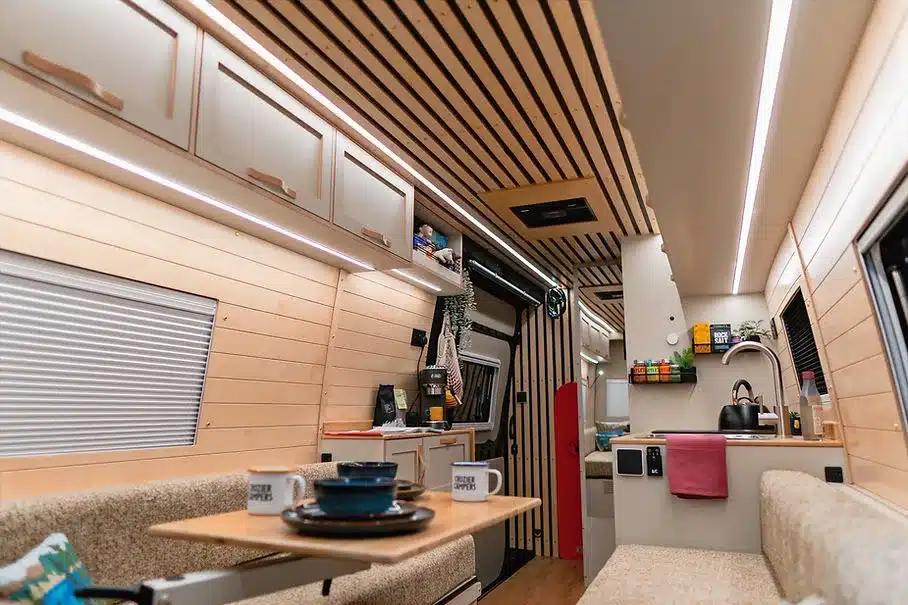 Innenansicht des Beyond 2 Campervan von Crozier Campers mit moderner Küche, Sitzgruppe und Holzverkleidung.