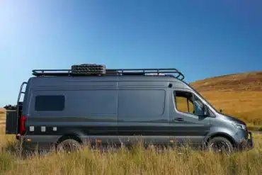 Seitliche Ansicht des Crozier Campers Beyond 2 Campervans in einer natürlichen Umgebung mit Dachträger und Ersatzreifen.