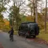 Schwarzer Beyond4 Campervan von Crozier Campers im Wald mit Fahrradfahrer auf der Straße.