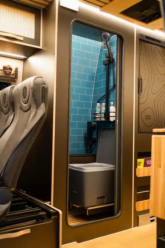 Dusche und Toilette im Beyond4 Kastenwagen von Crozier Campers, mit blauen Wandfliesen und modernen Armaturen.