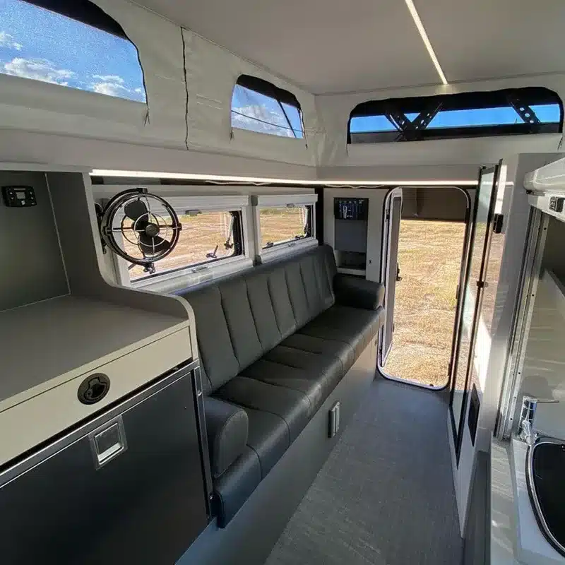 Blick in den Innenraum eines Black Rhino 2A Max Up Offroad-Caravans mit grauer Sitzbank, Fenstern und Pop-up-Dach