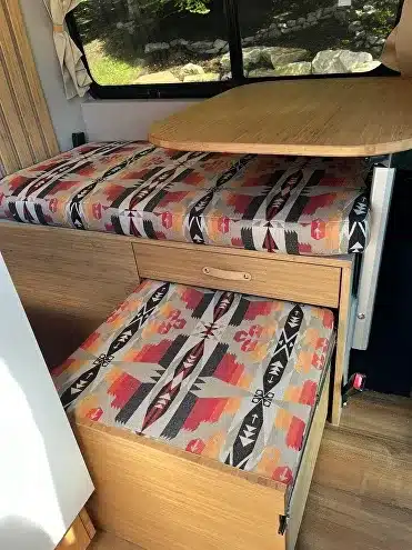 Sitz- und Schlafbereich mit farbenfrohen Polstern und Holztisch im kompakten Offroad-Caravan Black Rhino MINI 2A MAX.