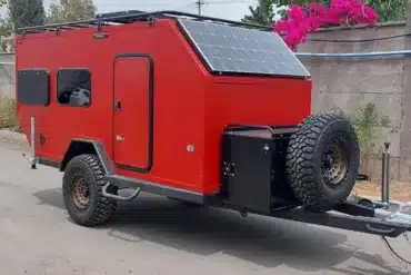 Roter Black Rhino MINI 2B MAX Offroad-Caravan mit Solarpanel und Ersatzrad auf Asphaltstraße