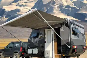 Black Rhino T11 Offroad-Caravan mit Markise vor schneebedecktem Berg, angehängt an ein Geländefahrzeug.
