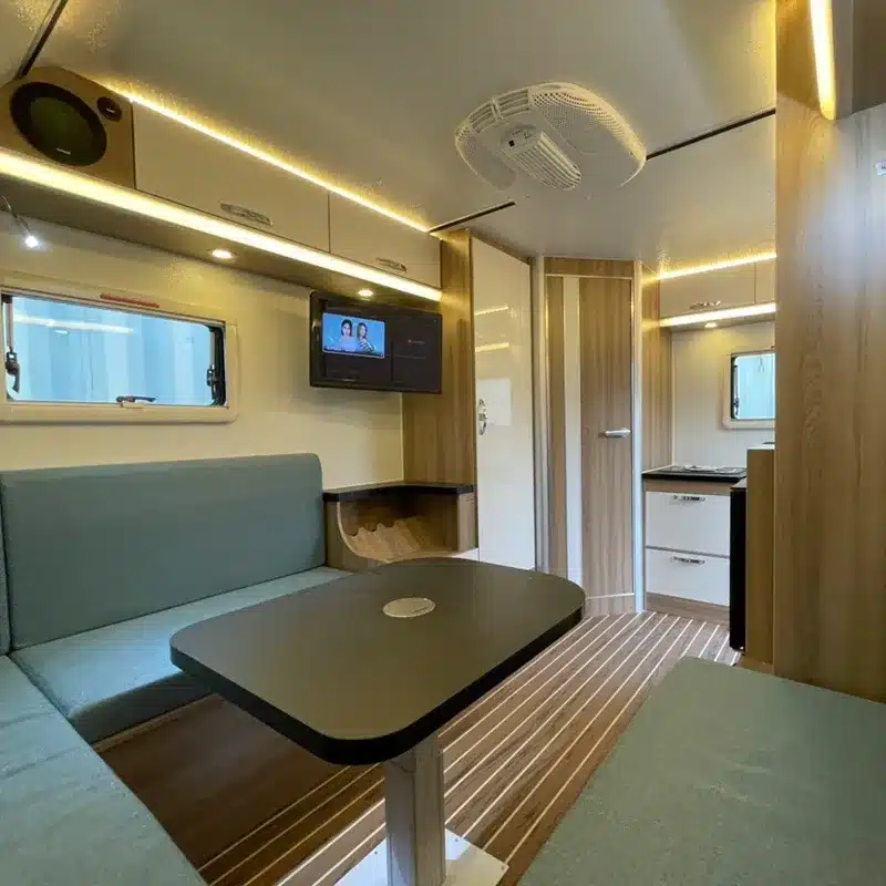 Innenansicht des Black Rhino T11 Offroad-Caravans mit U-förmiger Sitzgruppe, Tisch, Staufächern, Fernseher und Küchenzeile.