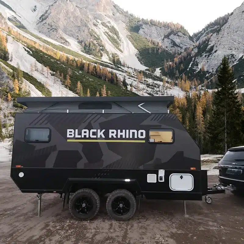 Black Rhino T12 Offroad-Caravan an einem SUV vor malerischer Bergkulisse, mit hoher Bodenfreiheit und markanter Outdoor-Optik.